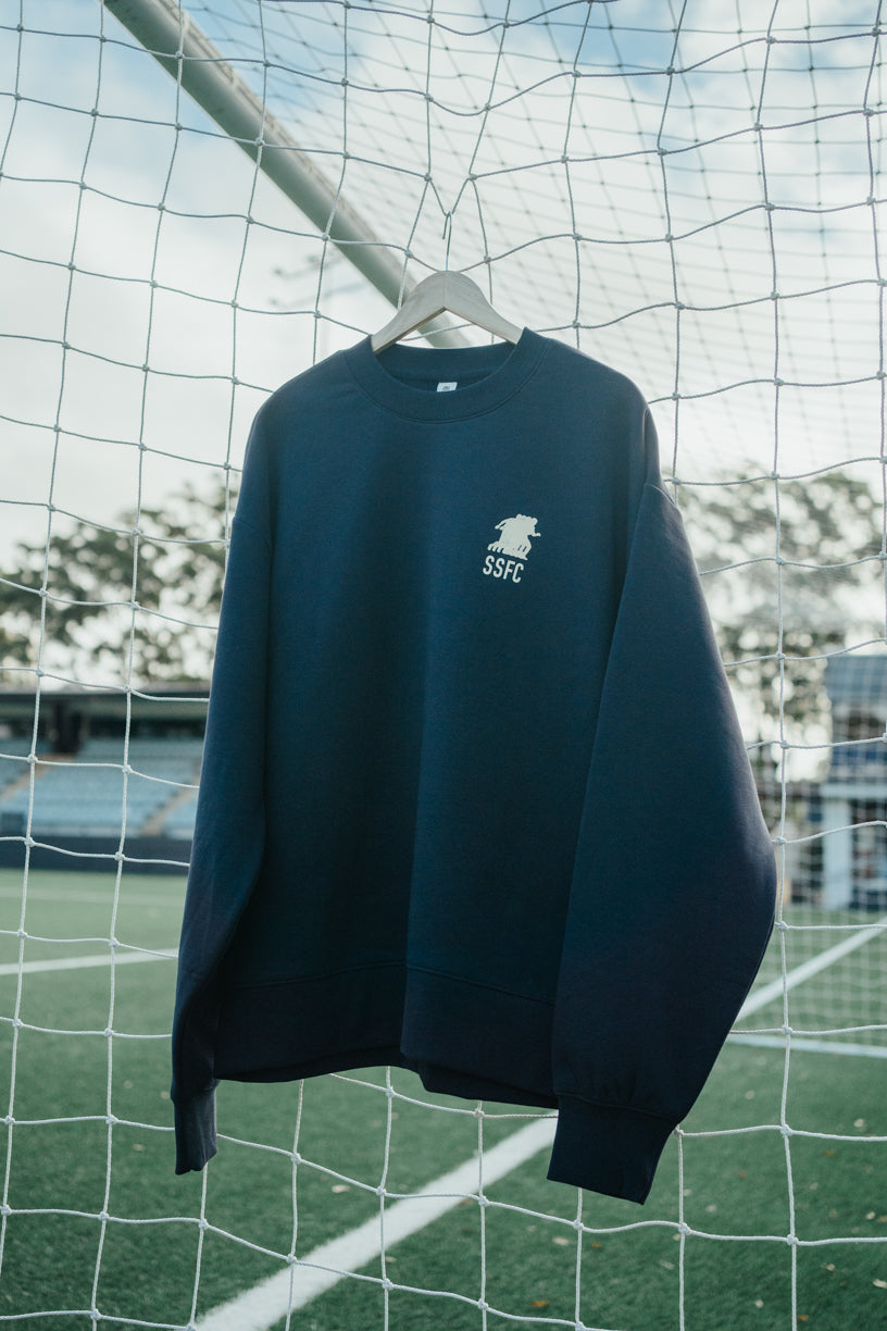 Navy blue sweatshirt with a logo on a hanger against a sports field background