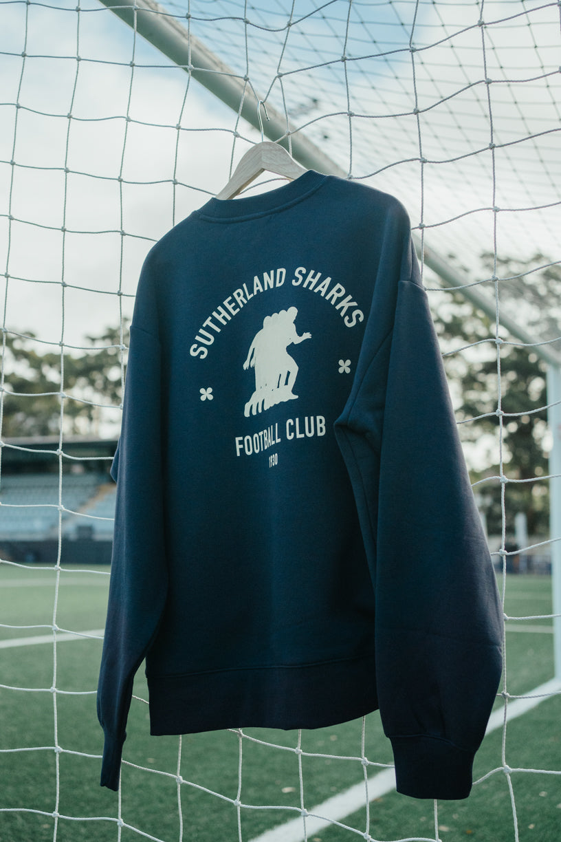 Navy blue sweatshirt with 'Sutherland Sharks Football Club' print hanging on a goalpost.