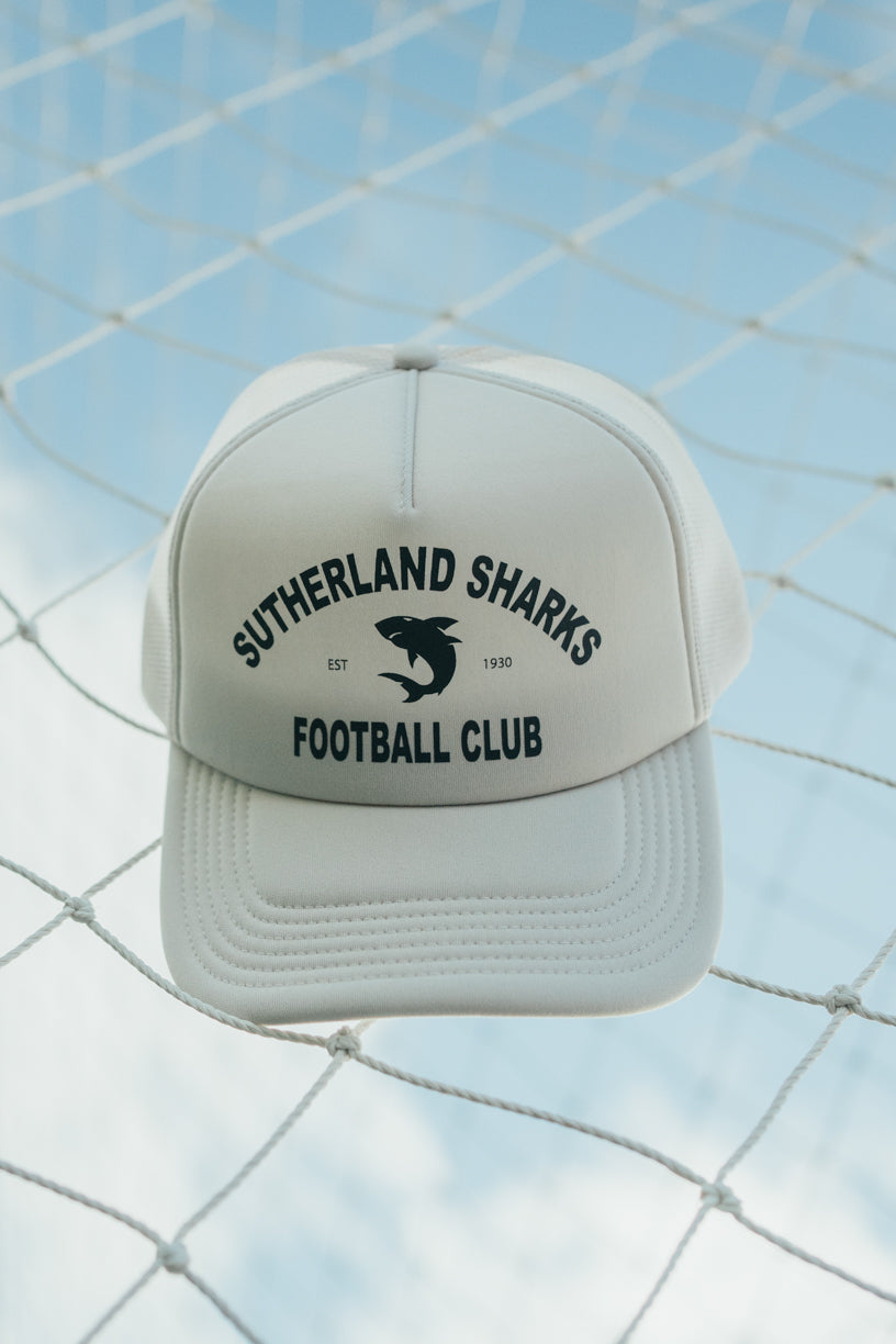 White cap with 'Sutherland Sharks Football Club' text and shark logo on a netted background